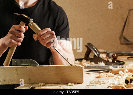 Carpenter carving wood with a chisel on a wooden bench Stock Photo