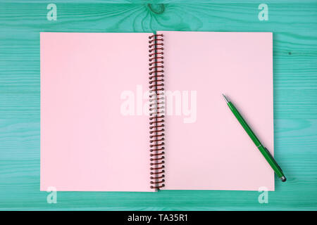 Pink blank page of an opened notebook and a green pen on the blue green wooden table Stock Photo