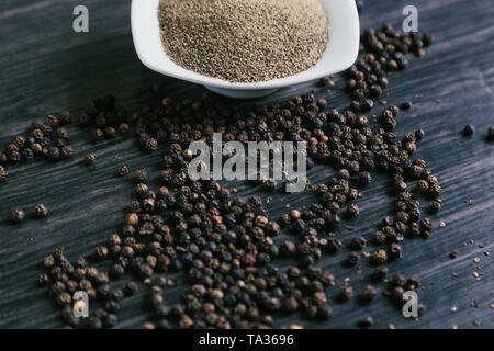 Black ground peppercorns in white bowl on wooden background. Stock Photo