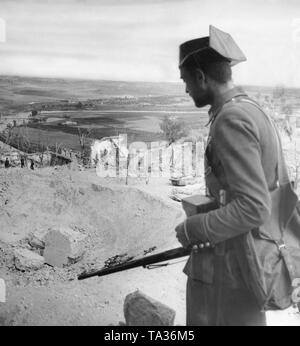 Photo of a Guardia Civil soldier (paramilitary police unit, which mostly joined the French troops in the Spanish Civil War), looks back on the ruins of the Alcazar of Toledo (Toledo fortress). In the background, the landscape. In the center, soldiers are running through the shell craters. Stock Photo