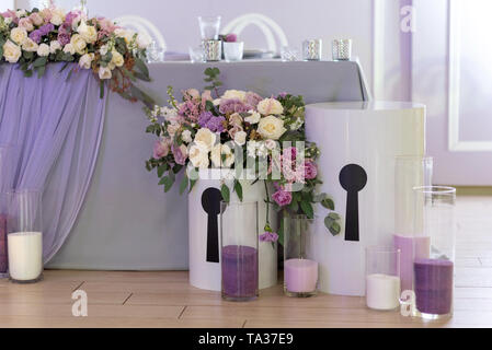 Original decoration of a zone near a wedding table of the groom and the bride. Big boxes with flowers. Candles in glass flasks on a parquet Stock Photo