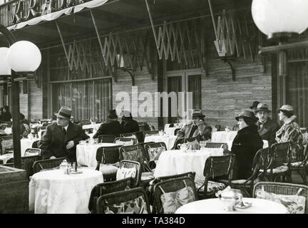 Some guests on the street terrace of the Cafe Kranzler in Berlin. The first Cafe Kranzler in Berlin was opened in 1825 by Johann Georg Kranzler as a small pastry shop in the street 'Unter den Linden' in Berlin Mitte. In 1932 he opened the second branch in the former Cafe des Westens under the name 'Restaurant und Konditorei Kranzler' in the Joachimstaler Strasse (today Joachimsthaler Strasse) in the district Charlottenburg. Both buildings were destroyed during air raids in the years 1944 and 1945. Stock Photo