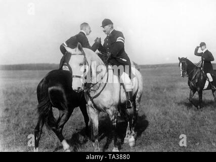 Crown Prince Wilhelm (left) and his father Emperor Wilhelm II (right) are shaking hands while sitting on their horses. Stock Photo