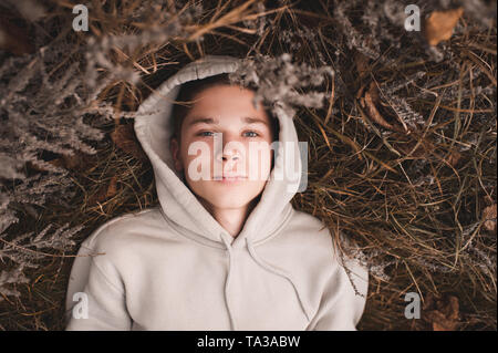 Sad teen boy 14-16 year old lying on groung wearing hoodie outdoors. Top view. Looking at camera. 20s. Stock Photo