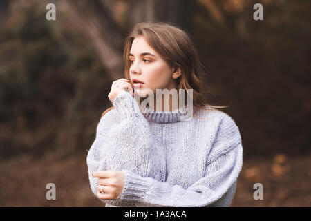 Stylish teen girl wearing knitted cozy sweater posing outdoors. Autumn season. 20s. Stock Photo