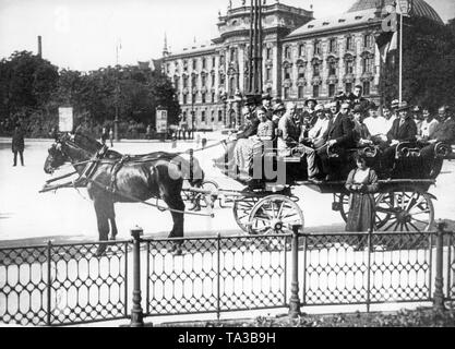 Tourists take a city tour with a horse-drawn carriage in Munich. In the background is the Palace of Justice on the edge of the Karlsplatz / Stachus. Stock Photo