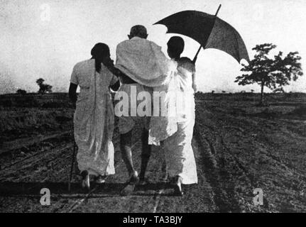 Mahatma Gandhi ; supported by two girls ; sharing a laugh with them ...