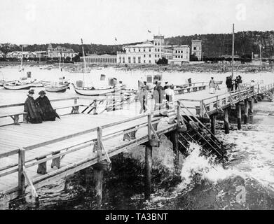 Holidaymakers on the pier in front of the seaside resort of Miedzyzdroje in Pomerania, on the beach are small sailing boats. Stock Photo