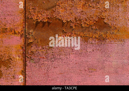 Red peeling paint on rusted sheet metal texture with vertical seam under direct sunlight Stock Photo
