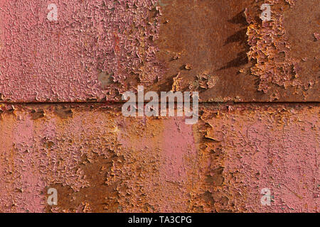 Red peeling paint on rusted sheet metal texture with horizontal seam under direct sunlight Stock Photo