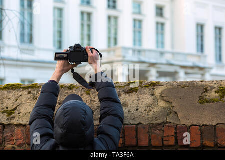 man in black cowl shooting with flip screeen dslr above the fence Stock Photo