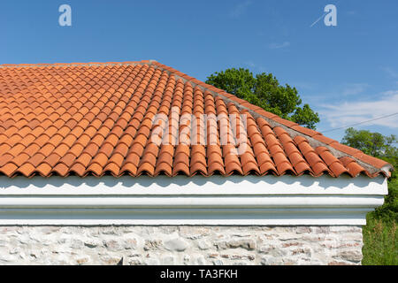 Red corrugated tile element of roof tile pattern over blue and cloudy spring sky day and green tree in the background. The roof on modern house Stock Photo