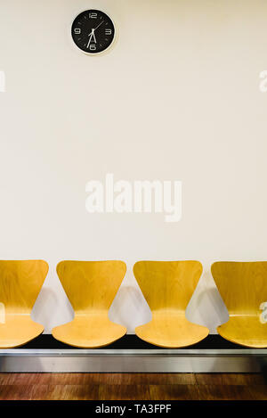 Waiting room with empty wooden chairs and wall clock, waiting concept. Stock Photo