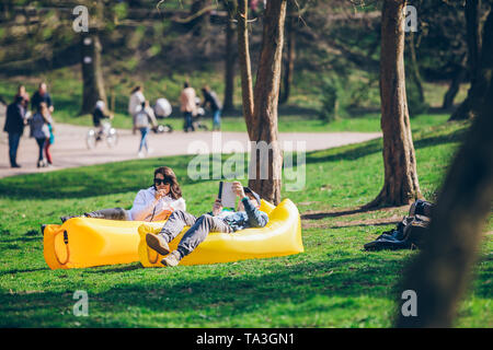 couple laying on yellow inflatable mattress in city park. reading book. drinking smoothies. leisure time Stock Photo