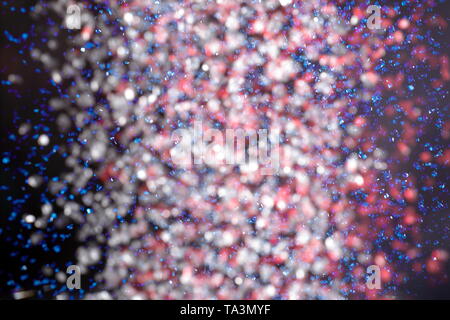 Mix of falling red, white, and blue sprinkles against a black background Stock Photo