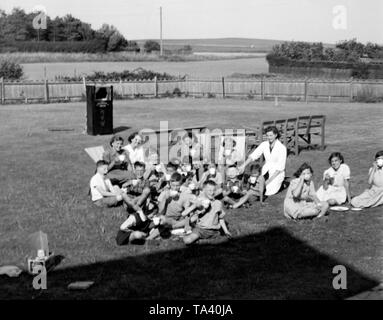 Children at Gracie Fields orphanage in Peacehaven, Sussex around 1956 having tea in the grounds in the background a Punch & Judy show is being set up Stock Photo