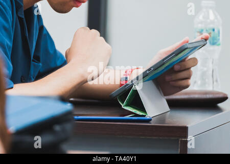 Close up of Asian student taking note on his tablet during a class. Concept of E-learning Stock Photo