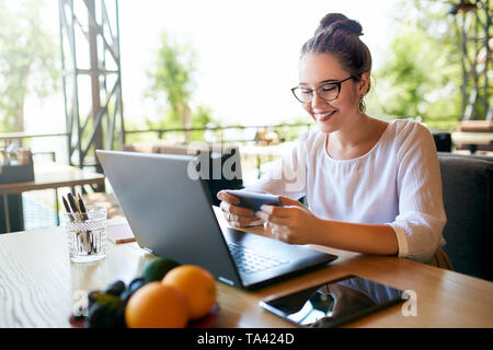Handsome businessman distracted from work on the laptop watching video on smartphone. Freelancer holding mobile phone and browsing using high speed 4g Stock Photo