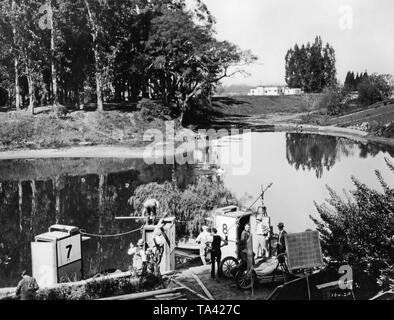 The camera crew of the first national Vitaphone movie 'The Careless Age,' directed by John Griffith Wray, is preparing the film set for a scene, in which Douglas Fairbanks Jr. as Wyn and Camel Myers as Ray sit in a canoe. Vitaphone was the name of a sound film system by the Warner brothers, which they used in around 2000 sound films. This system guarantees the simultaneity of image and sound in the film. A triple-soundproof camera box was used for the shooting. Stock Photo