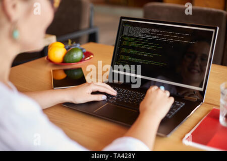 Back view over the shoulder shot of developer programmer with laptop. Program code and script data on the screen. Young freelancer in glasses working  Stock Photo