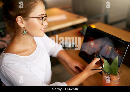 Freelancer retoucher woman works on convertible laptop computer with photo editing software using stylus. Photographer or designer performing digital  Stock Photo
