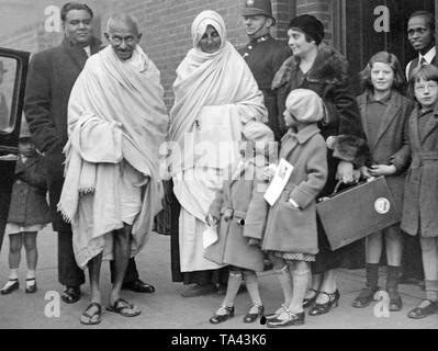 The leader of the Indian nationalist movement Mahatma Gandhi is invited to America by the President of the Indian Nationalist Association in America, Salandra Ghose. Salandra's daughter Mariam hands Gandhi the invitation. On the right next to Gandhi is his secretary Madeleine Slade, called Mirabeth, beside Salandra Ghose and her daughters Mariam and Lilabati. This shot was taken in front of Kingsley Hall, a community center in East London. Stock Photo