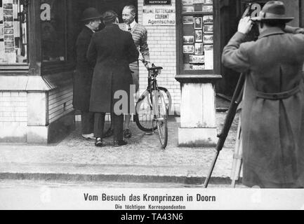 The Prussian Crown Prince (3rd from the left with bicycle) visits his father, the former Emperor Wilhelm II, in the Dutch town of Doorn. The occasion was the 67th birthday of the emperor in exile. Here, Crown Prince Wilhelm is interviewed and photographed by journalists in front of a shop. Stock Photo