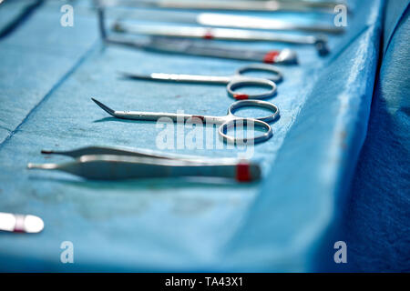 Close up of doctor hands during surgery in operation room. Sterile surgery instruments used in a real operation. Focus is on the row of clamp handles. Stock Photo