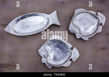 empty fish-shaped silver plates on a wooden table Stock Photo