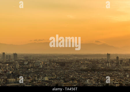 The iconic Mount Fuji rises above Tokyo southern suburbs wrappes in a yellowish evening mist Stock Photo