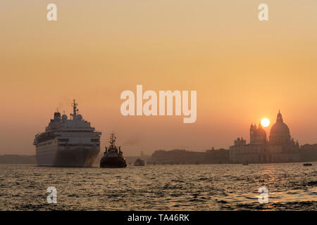 A tug boat tows a cruise ship in St. Mark's Basin at sunset in Venice Italy. Stock Photo