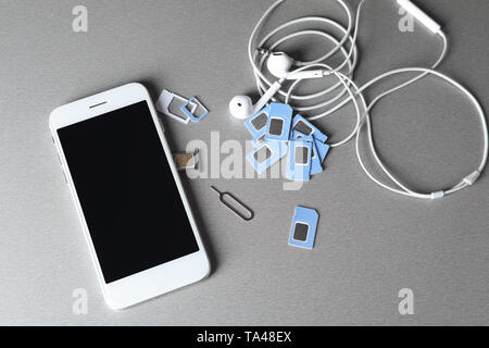 Mobile phone with sim cards and earphones on grey background Stock Photo