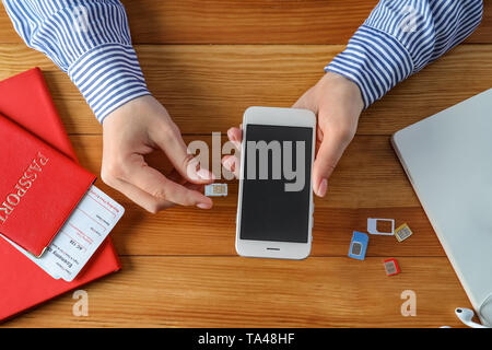 Woman inserting sim card into mobile phone on wooden table Stock Photo