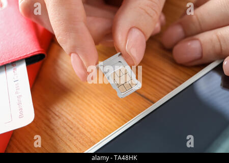Woman inserting sim card into mobile phone on wooden table, closeup Stock Photo