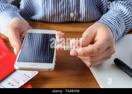 Woman inserting sim card into mobile phone at wooden table, closeup Stock Photo