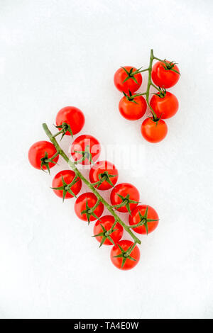 Cherry tomatoes on the vine on white textured and patterned background with copy space. Top view. Stock Photo