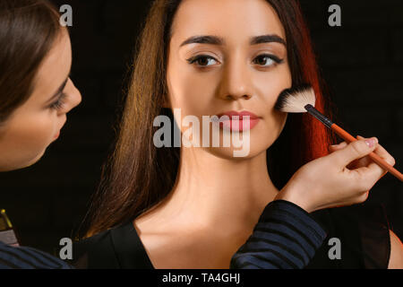 Professional makeup artist working with young model on dark background Stock Photo