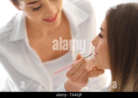Professional makeup artist working with young bride on light background Stock Photo