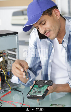 computer technician on the phone while he repairs a pc Stock Photo