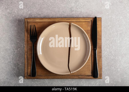 Cracked plate with cutlery and wooden board on grey background Stock Photo