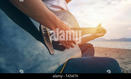 man's hands playing acoustic guitar, capture chords by finger on sandy beach at sunset time. playing music concept Stock Photo