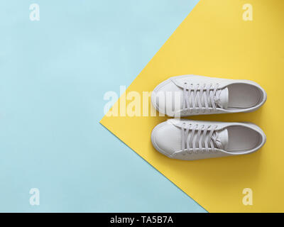 White leather sneakers on blue and yellow background. Pair of fashion trendy white sport shoes or sneakers with copy space for text on colorful backgr Stock Photo