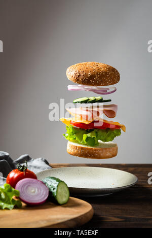 Flying ingredients burger or cheeseburger above the plate with ingredients on wooden cutting board on a dark background. Burger floating in the air ab Stock Photo