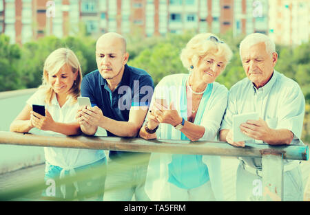 Portrait of positive mature couples using gadgets in park outdoor Stock Photo