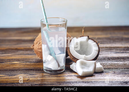 Coconut water in the composition with an open coconut with white flesh on a wooden background. Organic healthy dietary product widely used in cosmetol Stock Photo