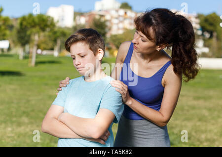 Offended tween boy standing on sports ground  while mom scolding him Stock Photo