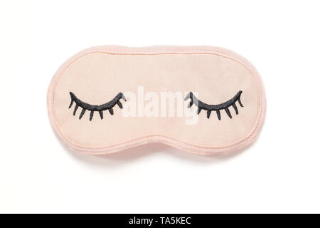 Pastel pink sleep mask with closed eyes embroidered on it with eyelashes on white background. Top view, flat lay. Concept of vivid dreams. Accessories Stock Photo