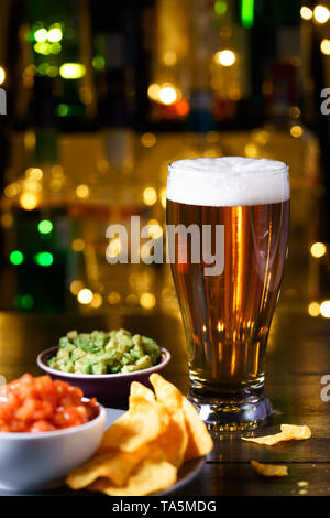 Glass of beer with nachos, tomato salsa and guacamole. Bar bottles in bokeh, high resolution Stock Photo