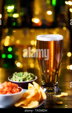 Glass of beer with nachos, tomato salsa and guacamole. Bar bottles in bokeh, high resolution Stock Photo
