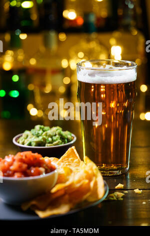 Glass of beer with nachos, tomato salsa and guacamole. Bar bottles in bokeh, high resolution Stock Photo